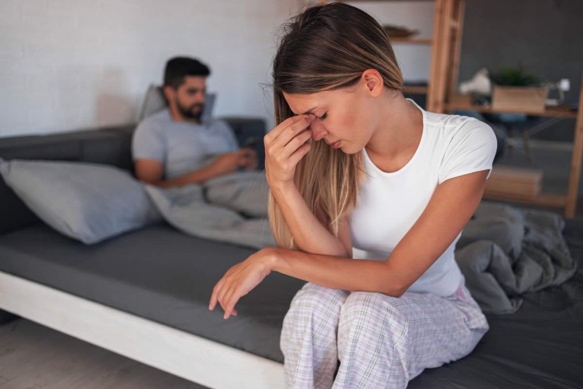 Donna seduta sul letto triste, uomo seduto sul lato opposto